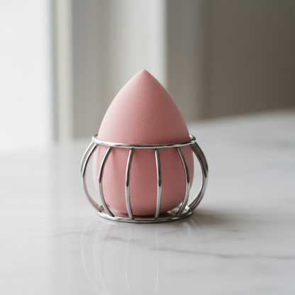 Close-up of soft pink makeup sponge sitting inside silver wire cage holder on white marble